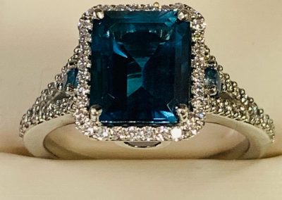 Blue topaz ring with diamond halo and intricate band design.